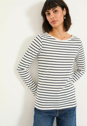Langärmliges gestreiftes Hemd in Weiß und Marineblau. Weicher Stoff mit weit ausgeschnittenem Hals und taillierter Silhouette. Kombiniert mit blauen Jeans.