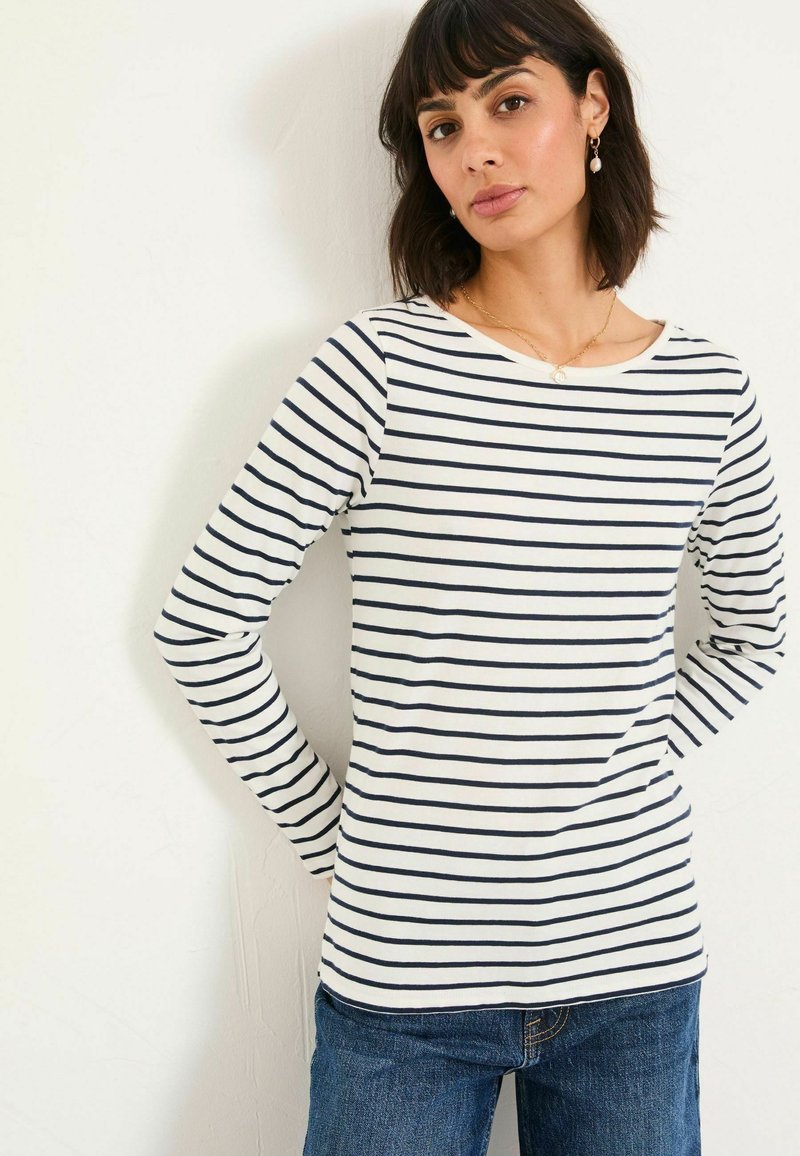 Langärmliges gestreiftes Hemd in Weiß und Marineblau. Weicher Stoff mit weit ausgeschnittenem Hals und taillierter Silhouette. Kombiniert mit blauen Jeans.