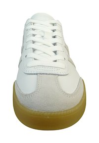 Zapatilla blanca con acentos de gamuza, cordones planos y una suela de goma. Presenta un diseño de punta redondeada limpio, sin marcas de la marca visibles.