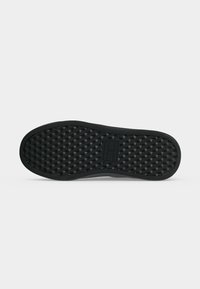 Semelle de chaussure noire avec un motif triangulaire texturé et une zone rectangulaire pour le logo au centre sur un fond clair uni.