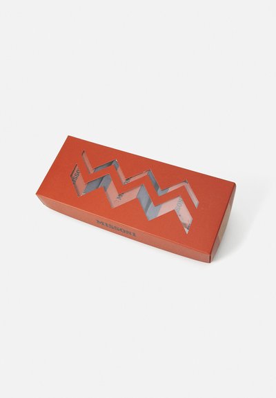 Rødt rektangulært emballasje med en sikksakk utskjæring. Har "MISSONI" i svart tekst. Inneholder mønstret materiale synlig gjennom utskjæringen.
