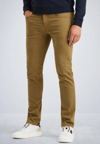 Chinos slim-fit en kaki avec un design à cinq poches, fabriqués en un mélange de coton doux et avec des coutures discrètes. Portés avec des baskets blanches.