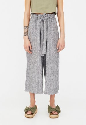 Woman wearing high-waisted, wide-leg gray ribbed pants with waist tie, olive green cropped top, and platform sandals with green bows.