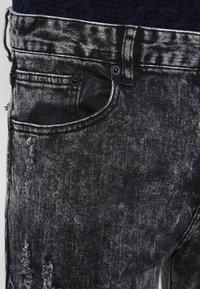 Czarne dżinsy z denimu o zniszczonej fakturze, lekko wyblakłe z widocznymi szwami i klasycznym krojem pięciu kieszeni.