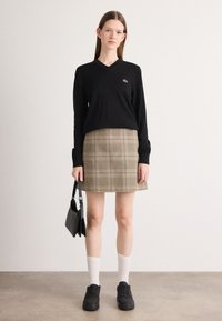 Maglione nero a scollo a V, gonna a quadri beige, calze bianche fino al ginocchio, sneakers nere, tiene una piccola borsa nera, texture lisce, fit sartoriale.