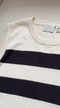 Sleeveless knit top with black and white horizontal stripes and ribbed neckline, laid flat on a textured beige surface.
