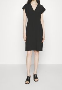 Svart klänning med V-hals, korta ärmar och en avslappnad passform, tillverkad av mjukt tyg. Matchad med svarta sandaler med halkskydd.
