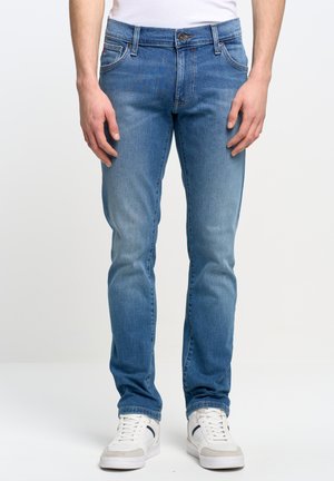 Jeans de denim azul claro con corte ajustado, que cuentan con cinco bolsillos, cierre de botón y cremallera, y un ligero desgastado en los muslos.