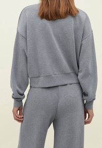 Felpa grigia con spalle cadenti, polsini e orlo a costine. Tessuto morbido con una vestibilità rilassata, abbinata a pantaloni grigi coordinati.