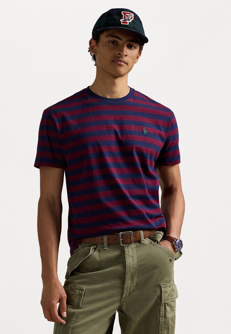 T-maica s prugami v mornarsko modri in maroon barvi iz bombaža, s krojaškim ovratnikom, v kombinaciji z olivnimi cargo hlačami in temno kapo z detajlom obliža.