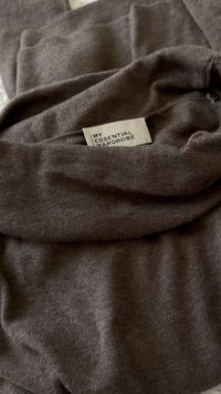 Dark brown, knit sweater with a funnel neck, featuring a care label reading "MY ESSENTIAL WARDROBE." Soft texture, folded fabric.