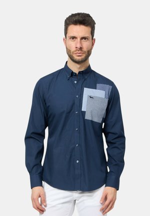 Camicia blu navy con un design testurizzato e tre accenti di tasca azzurri e lavorati sul petto. Tessuto morbido, maniche lunghe.