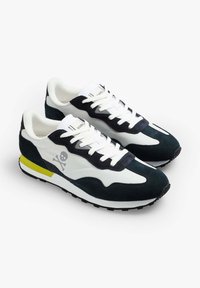 Sneaker navy e bianche realizzate in materiali scamosciati e in rete, con un accento giallo, design con lacci e un logo a forma di teschio sul lato.