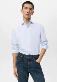 Camicia a maniche lunghe a righe blu chiaro con colletto button-down, abbinata a jeans in denim scuri. Caratterizzata da una vestibilità comoda e maniche arrotolate.