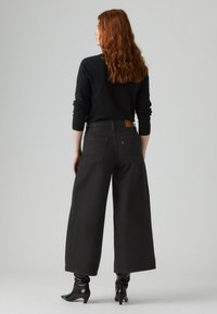 Svarte vide jeans med høy midje, baklommer og lærdetalj bak. Kombinert med en svart langermet topp og ankelstøvler.