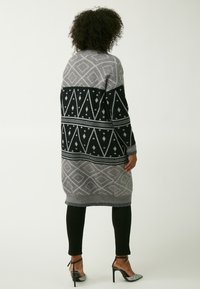 Cárdigan largo con un patrón geométrico en gris y negro, que presenta una mezcla de diseños de diamantes y triángulos, textura de punto y puños acanalados.