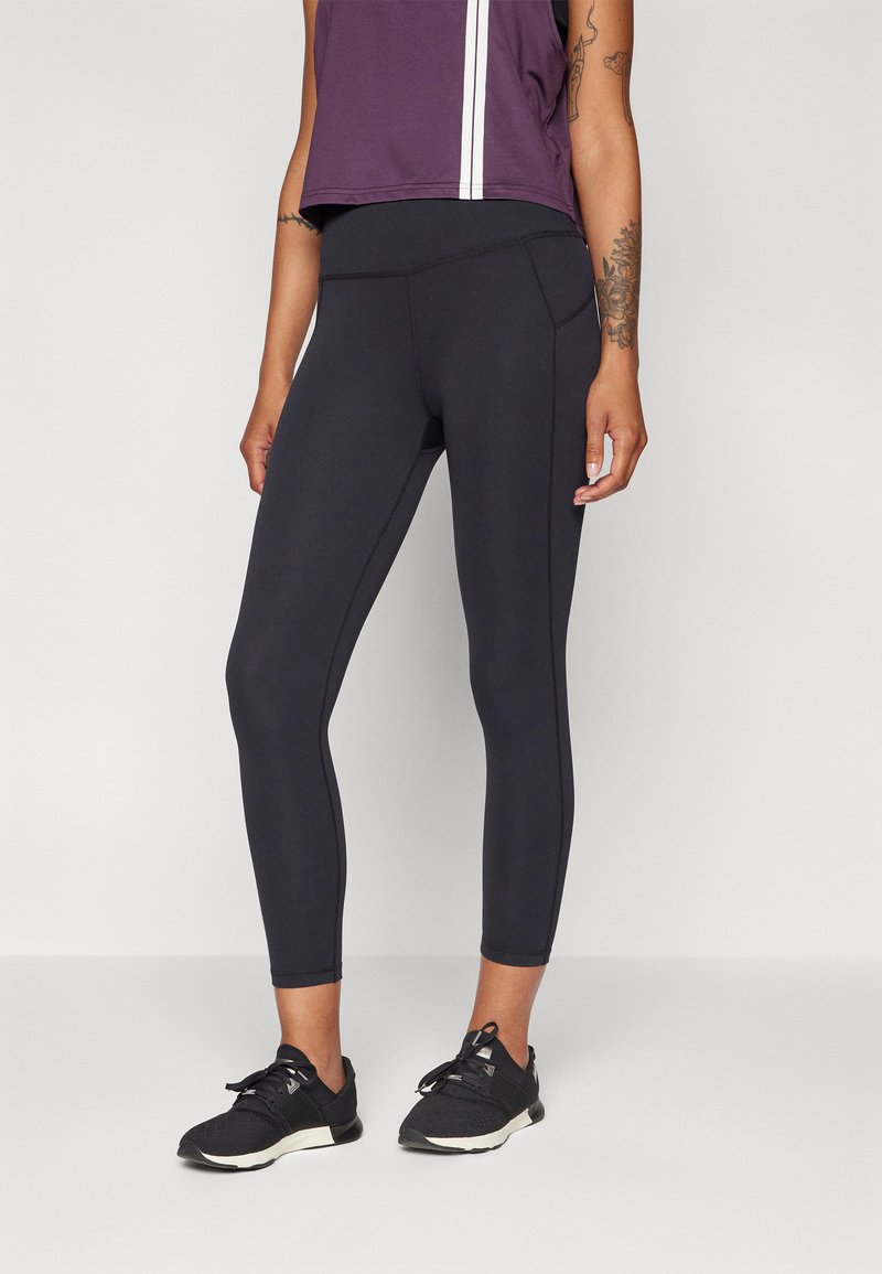 Fekete leggings, kontrasztos varrással és magas derékkal, lila crop top-pal párosítva, fehér csíkokkal. Strukturált anyag.