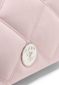 Vadderad ljusrosa läderväska med en rund silverlogo, stitching detaljer och en slät yta.