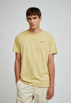 Lys gul kortærmet t-shirt med rund halsudskæring. Har et lille brunt tekstlogo på brystet. Fremstillet af et blødt, tekstureret stof.