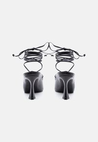 Ζευγάρι μαύρα ψηλοτάκουνα παπούτσια με μυτερές φτέρνες και μακριά λεπτά λουριά που τυλίγονται και δένουν στον αστράγαλο, από πίσω.