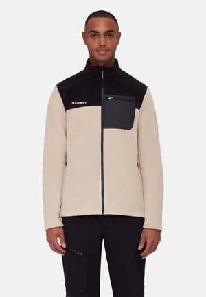 Fleece jacket in cream and black with a zip front, high collar, and chest pocket. Features logo on the left side. Smooth texture.
