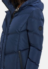 Navyblauwe gewatteerde jas met een capuchon, met een gladde, glanzende textuur, een ritszak aan de zijkant en een ronde logo op de mouw.