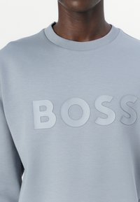 Felpa grigia chiara con colletto a girocollo e logo "BOSS" testurizzato di una tonalità leggermente più scura, realizzata in tessuto morbido e liscio.