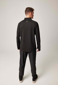 Schwarzes Sportoutfit mit langärmligem Oberteil und passender Hose, mit figurbetontem Schnitt und glatter Textur. Enthält ein minimalistisches Logodetail.