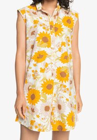 Vestido sin mangas hecho de una tela ligera, con un patrón brillante de girasoles y flores en amarillo, naranja y verdes suaves; cierre de botones al frente.