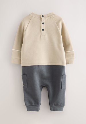 Beige cotton sweatshirt with black buttons and gray cotton pants featuring side pockets and embroidered letter R. Smooth texture and structured design.