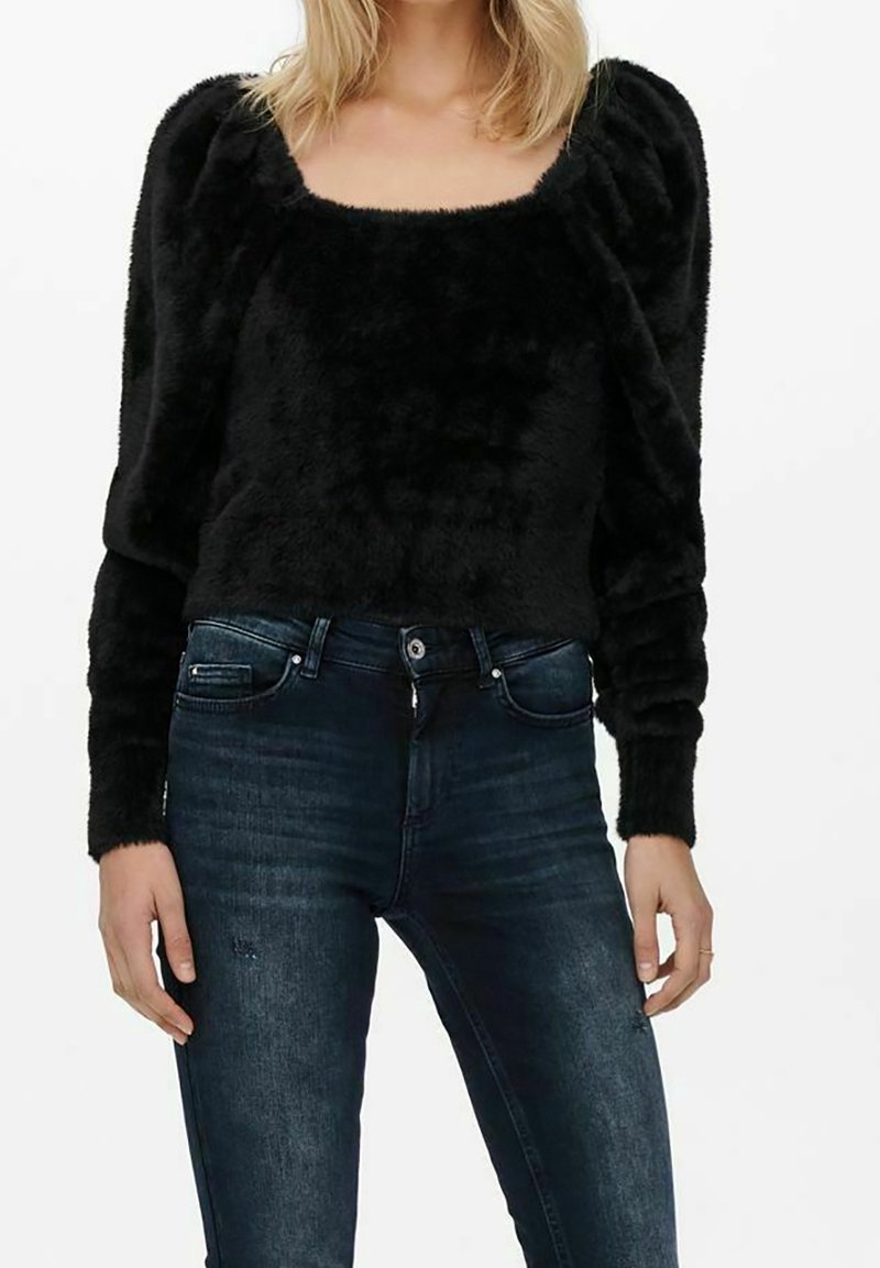 Un pull noir en peluche avec un col carré et des manches bouffantes, associé à un jean en denim bleu foncé. Les matériaux semblent doux et texturés.