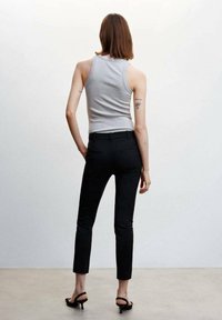 Grijze geribbelde tanktop gecombineerd met strakke zwarte broeken. Het model draagt zwarte hoge hakken. Minimalistisch ontwerp, gladde textuur en strakke lijnen.