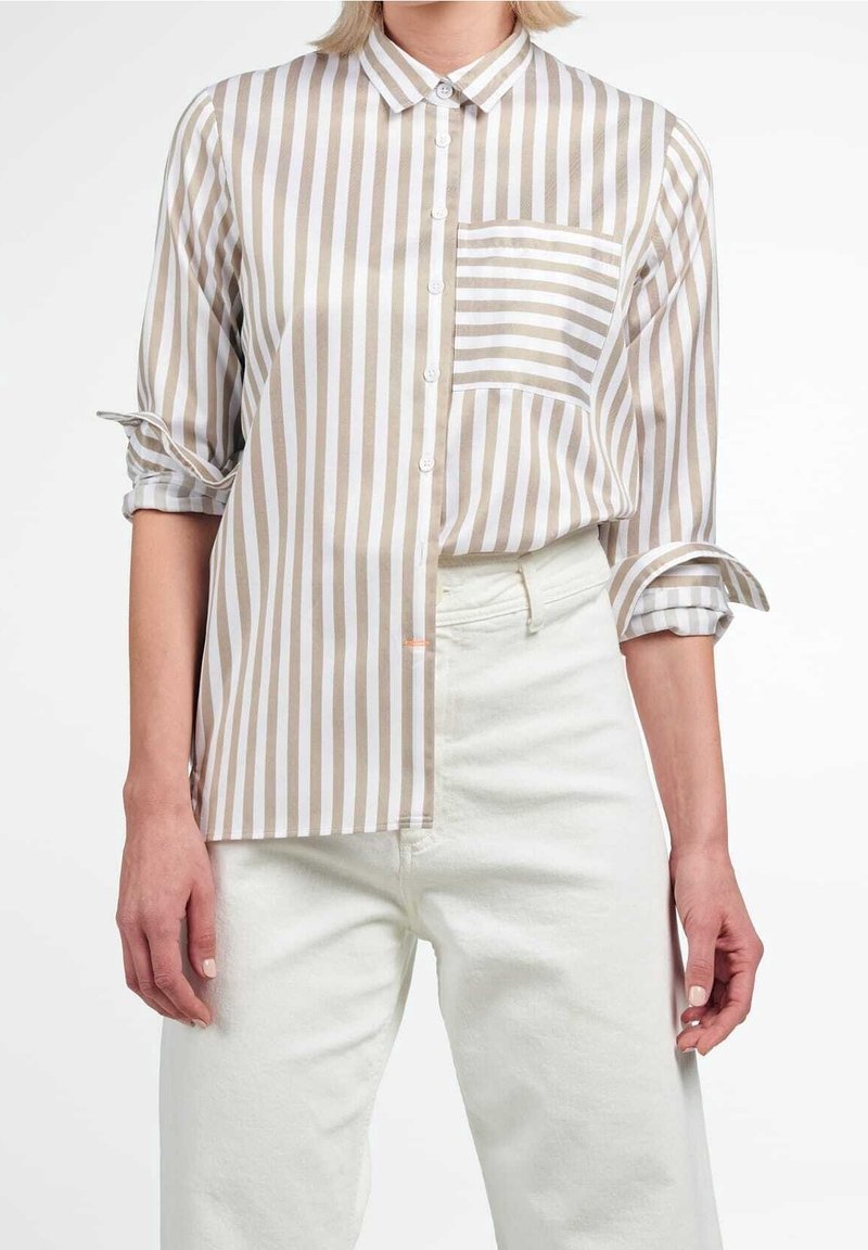 Camicia a righe beige e bianca, con tasca, maniche arrotolate e una texture di tessuto liscia. Abbinata a pantaloni avorio.