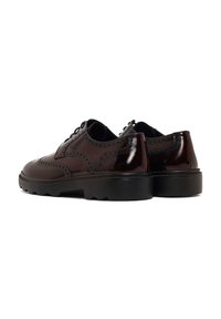 Zapatos de charol marrón con detalle de brogue, puntera redondeada y suela gruesa de goma negra con patrones de agarre.