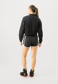 Sweatshirt noir court à manches longues accompagné de shorts noirs avec des accents blancs. Porté avec des chaussures de sport noires.