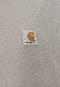 Ύφασμα γκρι ανοιχτό φούτερ με υφασμένο ορθογώνιο ετικέτα που παρουσιάζει πορτοκαλί και λευκό λογότυπο. Ομαλή υφή, καθημερινό σχέδιο.