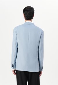 Helles blaues Blazer mit strukturierter Passform, einem Schlitz hinten und schwarzen Knöpfen an den Ärmeln. Hergestellt aus glattem, strukturierte Stoff.
