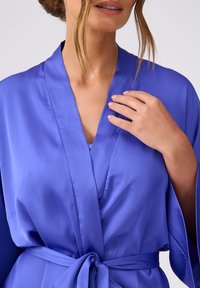 Jedwabna, niebieska szata z głębokim dekoltem w kształcie V i szerokimi rękawami, z wiązanym w pasie. Gładka tekstura z minimalnym połyskiem, prezentująca eleganckie drapowanie.