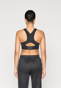 Μαύρο αθλητικό σουτιέν με σχεδιασμό racerback, ανοιχτή λεπτομέρεια κοπής και ρυθμιζόμενο κούμπωμα με αγκράφα στο πίσω μέρος, συνδυασμένο με μαύρο παντελόνι φόρμας.