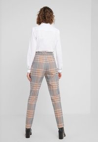 Pantalons à carreaux gris avec des lignes orange, dotés d'une taille haute et d'une coupe ajustée, associés à une chemise blanche et des bottes à talons carrés noires.