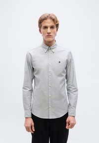 Ανοιχτό γκρι πουκ άμισο με κουμπιά και μακριά μανίκια, με μυτερό γιακά, που διαθέτει μικρό μαύρο λογότυπο στο αριστερό στήθος, κατασκευασμένο από λείο ύφασμα.