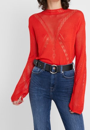 Red knitted sweater with a textured pattern and long sleeves, paired with dark blue jeans and a black belt featuring a round buckle.