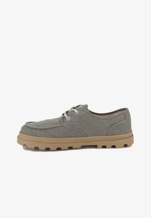 Zapatillas de lona gris con punta redondeada, suela de goma beige contrastante y ojales claros para los cordones. Diseño ligero con parte superior texturizada.