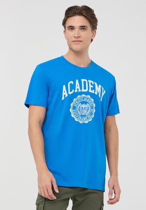T-shirt in cotone blu con una grafica bianca con il testo "ACADEMY" e il suo sigillo sulla parte frontale. Design classico con collo rotondo, maniche corte e vestibilità regolare.