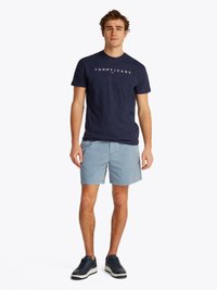 Mørkeblå bomulls t-skjorte med "TOMMY JEANS"-logo, lyseblå shorts og mørke sneakers med hvite detaljer. Enkle, avslappede klær.