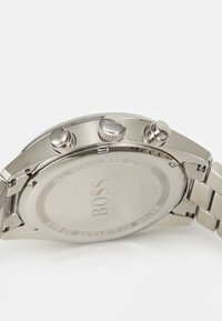 Roostevabast terasest kroonograafkell, millel on poleeritud viimistlus, kaks nupuvajutust, tekstuuriga kroon ja graveeritud logo tagaküljel.