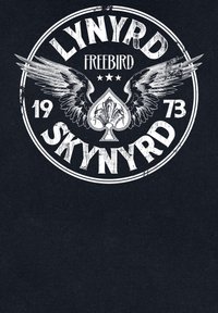 Gráfico negro que presenta el texto "LYNYRD SKYNRYD FREEBIRD 1973" con ilustraciones de alas y trébol, letras blancas desgastadas, diseño circular.