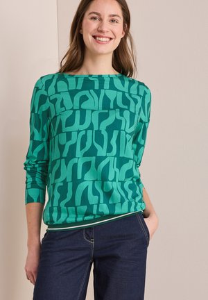 T-shirt vert à manches longues avec un motif abstrait audacieux, col rond et tissu doux. Associé à un jean foncé, mettant en valeur un look décontracté.