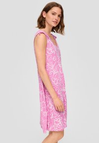 Abito floreale rosa con scollatura a V, design senza maniche e lacci decorativi sulle spalline. Realizzato in tessuto morbido, presenta motivi floreali bianchi.