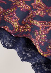 Tamsiai mėlynas audinys su paisley raštu raudonos, geltonos ir oranžinės spalvų. Juodas nėrinių apvadas palei kraštą su banguotu dizainu.